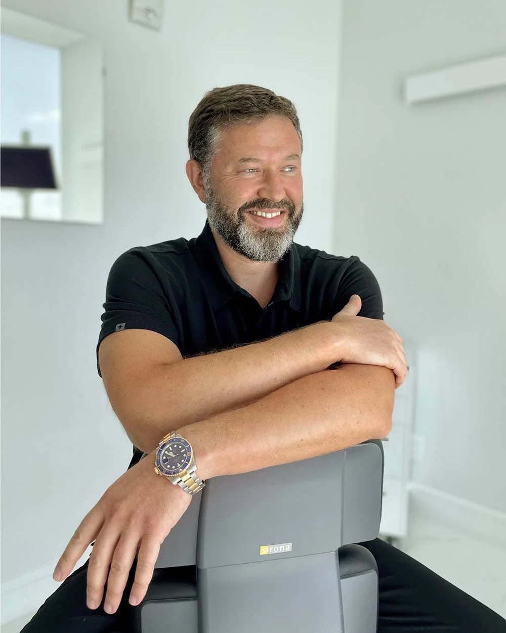 Dr. Baruch Tetri, smiling, leaning on a dental chair in the Sunny Isles clinic